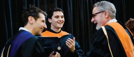 Three people smiling in a candid commencement picture.